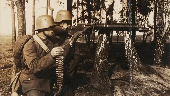Das Foto zeigt zwei Soldaten an einem Maschinengewehr im Wald.