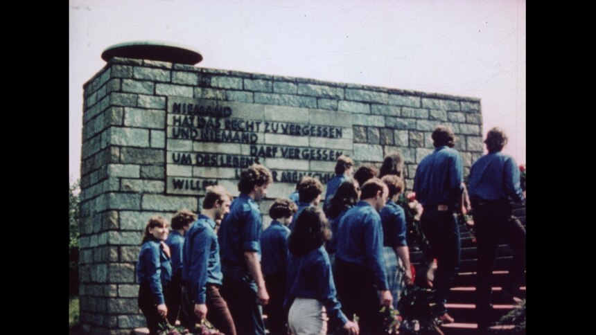 Eine Menschengruppe, einheitlich bekleidet mit blauen FDJ-Hemden, besteigt eine Treppe zu einem Mahnmal.