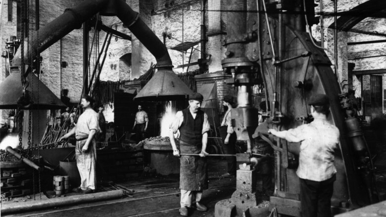 Das Foto zeigt eine Werkhalle mit mehreren Arbeitern an Maschinen.