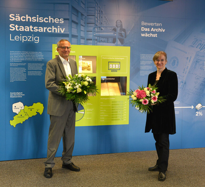 Zwei Personen mit Blumensträußen vor Ausstellungswand